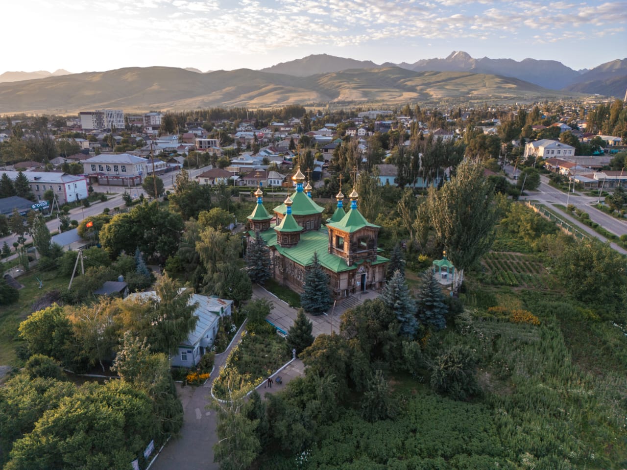 Holy Trinity Cathedral in Karakol from above: green roofs among the trees, the city and the Terskey Ala-Too mountains
